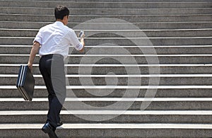 Businessman holding mobile and in hurry to run up on stairs