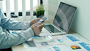 Businessman holding a mobile smartphone work on a laptop computer Analyzing, calculating, graphing, business data in the office, r