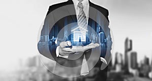 Businessman holding modern buildings hologram, and home icon. Real estate business, building technology and smart home concept