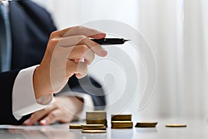 Businessman holding a pen and pointing something with stack of gold coin. Investment and financial management concept