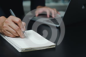 Businessman holding pen writing book note on desk with computer laptop