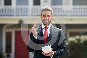 Businessman holding piggy bank on home house background. Handsome caucasian man holding piggybank for money for savings.