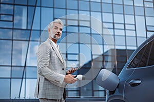 Businessman holding power supply cable at electric vehicle charging station.