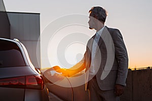 Businessman, holding power supply and charging his electric car during sunset. Concept of ecology tranport. photo