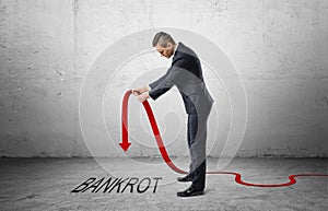 Businessman holding red line graph with downturned arrow which is pointing to the word 'bankrot'