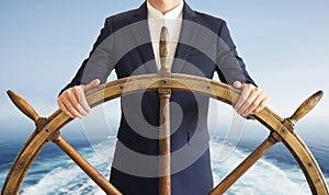 Businessman holding ship rudder with blue sea on background.