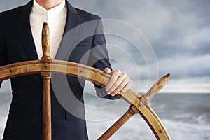 Businessman holding ship rudder and navigates in storm