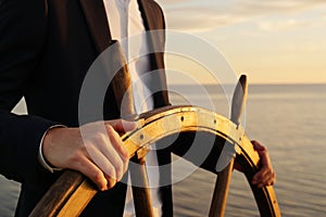 Businessman holding ship rudder and navigates in sunset light