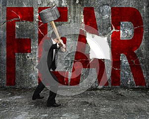 businessman holding sledgehammer hitting red FEAR word on concrete wall