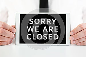 Businessman holding a smart tablet with sign Sorry We Are Closed