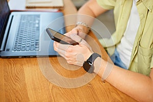 Businessman holding smartphone sitting in office, using cell phone mobile apps and laptop