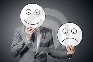 Businessman holding smile and sad mask. Conceptual image of a man changing his mood from bad to good