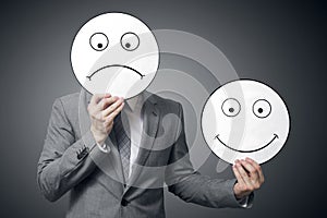 Businessman holding smile and sad mask. Conceptual image of a man changing his mood from bad to good