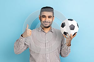 Businessman holding soccer ball on his hand with smiling positive expression, showing thumb up.