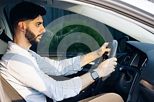 Businessman holding steering wheel while driving modern electric car on the street road. Confident man driving expensive