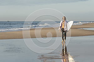 A Businessman holding is surfboard walking along the beach