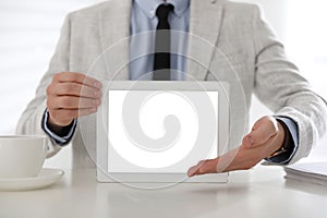 Businessman holding tablet with blank screen at white table in office, closeup