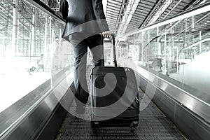 Businessman holding trolley bag going up on airport escalator