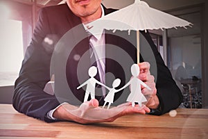 Composite image of businessman holding umbrella and paper family