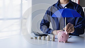 Businessman holding umbrella on pile of money, coins and piggy bank concept Financial insurance