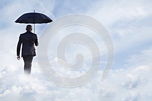 Businessman holding an umbrella and walking away in dreamlike clouds