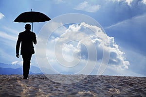 Businessman holding an umbrella and walking away in the middle of the desert with dreamlike clouds photo