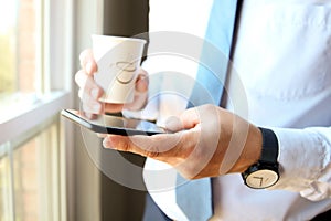 Businessman holding and using the mobile smart phone. Cup of cofee or tee