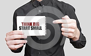Businessman holding a white notepad with text THINK BIG START SMALL, business concept