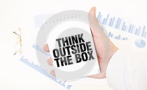 Businessman holding a white notepad with text THINK OUTSIDE THE BOX, business concept