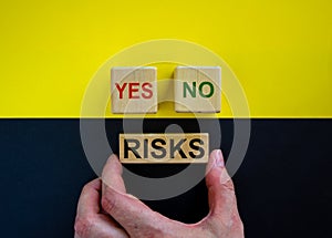 Businessman holds a block with word `risks`. Wooden cubes with  words `yes, no`. Beautiful yellow and black background. Copy s