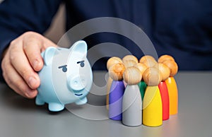 A businessman holds a blue piggy bank next to a group of people figures.