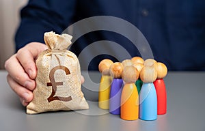 A businessman holds a british pound sterling money bag near a group of people figurines.