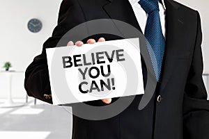 Businessman holds a card with the message believe you can