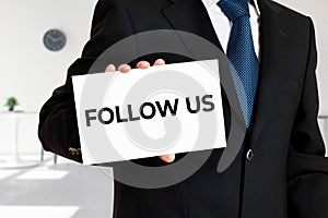 Businessman holds a card with the word follow us