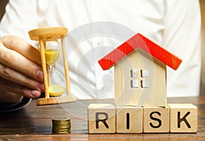 Businessman holds clock, wooden house and the inscription Risk on wooden block. The concept of non-payment of interest rates on