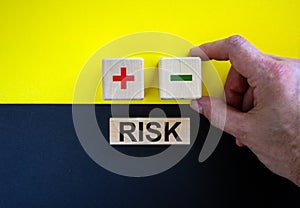 Businessman holds a cubes with minus icon. Wooden cubes with  word `risk`. Beautiful yellow and black background. Copy space.