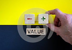 Businessman holds a cubes with plus icon. Wooden cubes with  word `value`. Beautiful yellow and black background. Copy space.