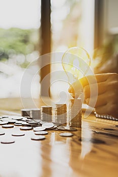 Businessman holds a glowing light bulb on top of the highest pile of coins, Placing coins in a row from low to high is comparable