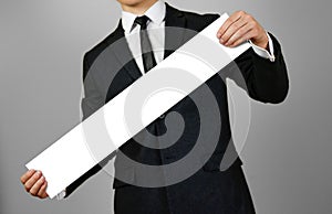 Businessman holds in hands a long, narrow paper. Empty for your text. Isolated on gray background.