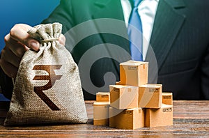 Businessman holds indian rupee money bag and boxes with goods. Import and export. Business income. Payment of taxes and fees.