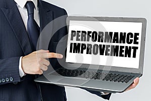 A businessman holds a laptop in his hands and shows on the screen with the text - PERFORMANCE IMPROVEMENT