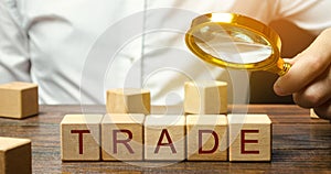 Businessman holds a magnifying glass over the word Trade. Business market and finance concept. Transfer of goods or services.