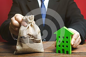 Businessman holds a money bag near a wooden house. Real estate investing concept. Developer. Taxes, mortgage, loan. Planning and