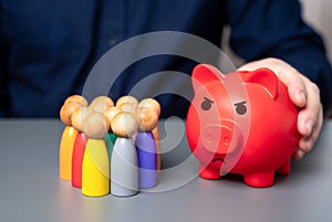 A businessman holds a red piggy bank next to a group of people figures. photo