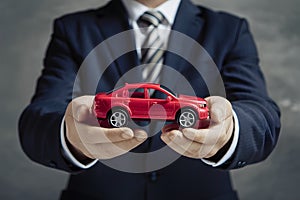 Businessman holds red toy car, illustrating car purchase concepts