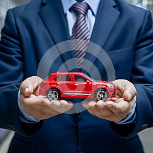 Businessman holds red toy car, illustrating car purchase concepts