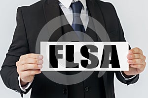 A businessman holds a sign in his hands which says FLSA