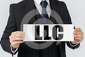 A businessman holds a sign in his hands which says LLC - LIMITED LIABILITY COMPANY