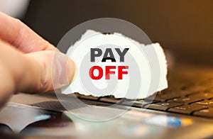 Businessman holds torn paper with the words PAY OFF on the background of the computer