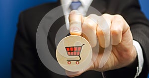 Businessman holds a wooden block with the image of a supermarket cart - shopping trolley. Retail and shopping. Ecommerce and